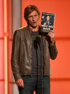 Denis Leary holds his 2008 book, ‘Why We Suck’ on stage in NYC, Sept. 5 