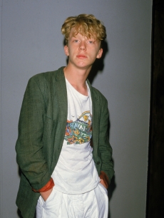Anthony Michael Hall poses for a photograph as he wears a t-shirt and a jacket with the sleeves rolled up, Hollywood, California, late 1980s